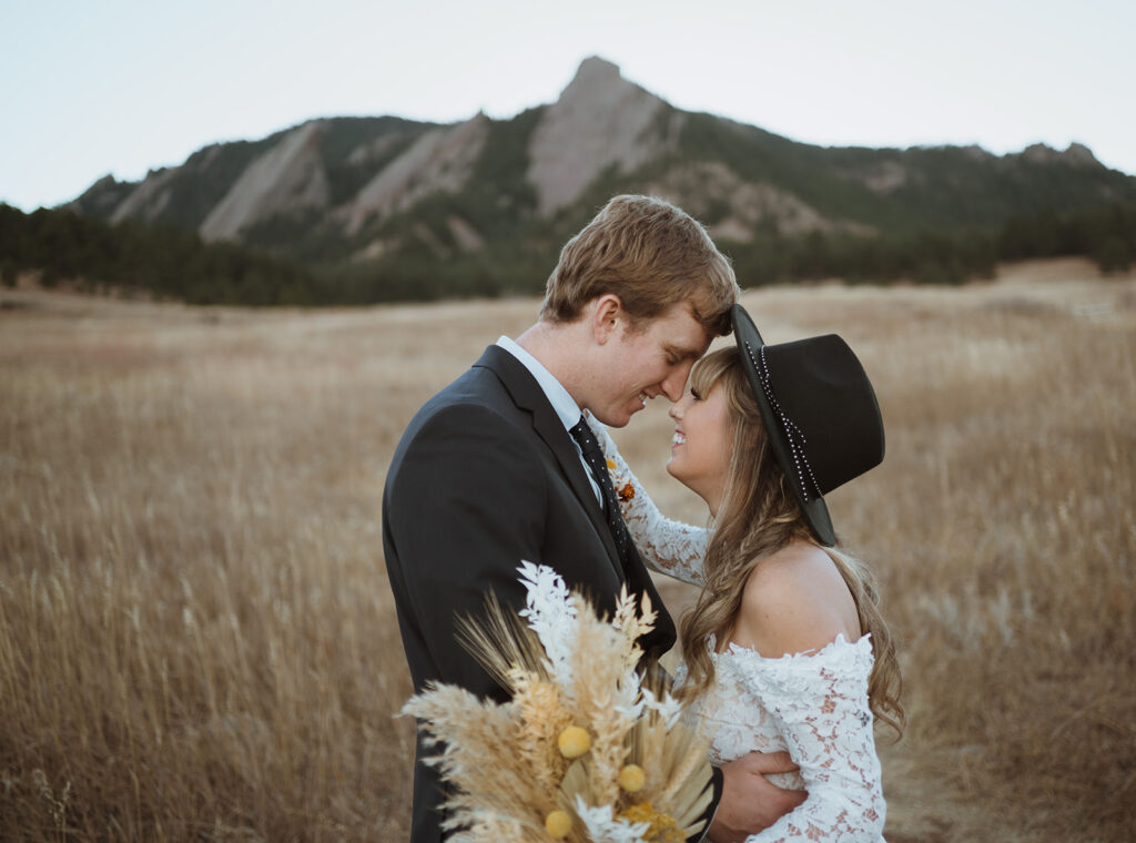 The bride and groom have their foreheads pressed together. They eloped in boulder for their colorado elopement. The bride has her flowers out of focus in the camera and the flat irons are in the background and they are green and grey.